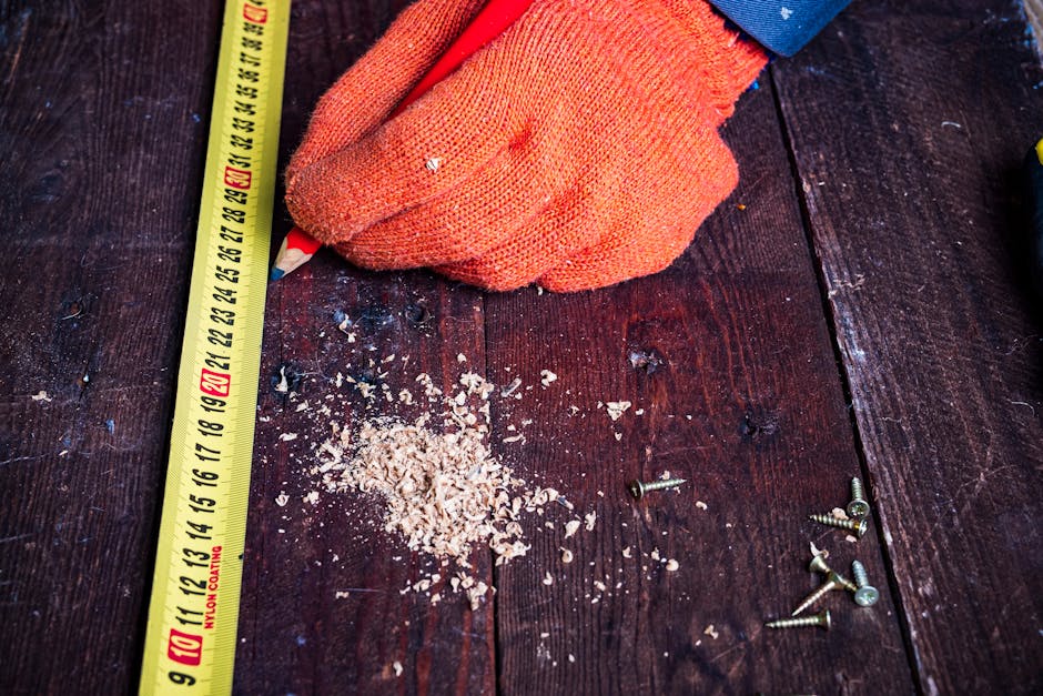 Carpenter measuring wood with measuring tape, pencil, and screws on workbench.